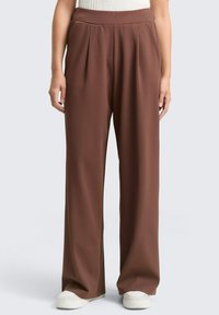 Wide-leg trousers in rich brown fabric, featuring pleats at the front, a high waist, and side pockets. Styled with white sneakers.