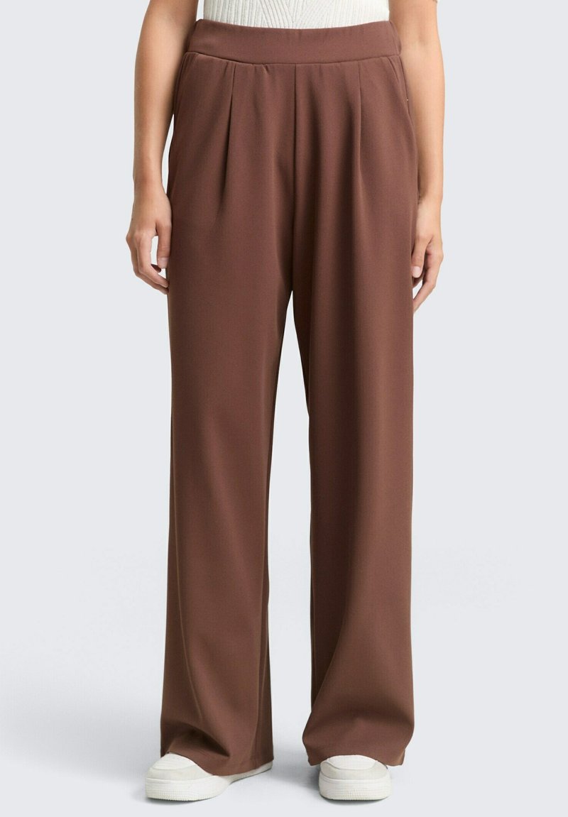 Wide-leg trousers in rich brown fabric, featuring pleats at the front, a high waist, and side pockets. Styled with white sneakers.