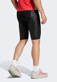 Zwarte sportshorts met een textuur van golven, gecombineerd met grijze sneakers met roze accenten en witte sokken.