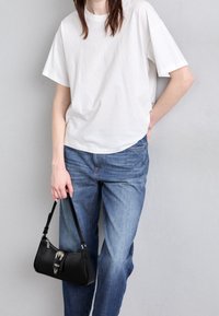 Bílý bavlněný tričko, volný střih, spárované se světle modrými džíny. Černá kabelka s zakřiveným tvarem a stříbrnými detaily.