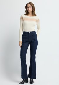 Kremowa, prążkowana bluzka z długim rękawem o teksturowanym wzorze, w połączeniu z ciemnoniebieskimi, wysokogatunkowymi dżinsami w kształcie dzwonów z małymi kropkami oraz czarnymi botkami za kostkę.