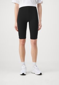 Shorts neri da biker realizzati in tessuto elasticizzato, con vita alta e finitura liscia. Abbinati a scarpe e calze sportive bianche.