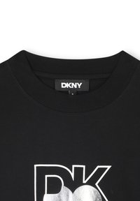 Camiseta negra de DKNY con cuello redondo, material de algodón suave y un gran logo gráfico plateado en el centro. Detalles de costura mínimos.