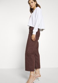 Sweatshirt branco cropped combinado com jeans de perna larga em bordeaux de cintura alta. A modelo usa sandálias brancas de salto alto com tiras.