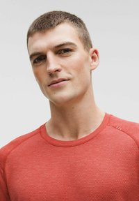 Tricou roșu cu mâneci scurte, cu un model texturat tricotat, guler rotund și mâneci raglan. Material neted, cu detalii subtile în zona umerilor.
