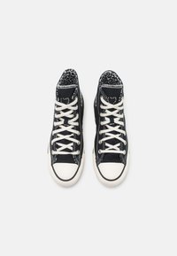 Zapatillas altas de lona negra con cordones blancos, puntera de goma y un forro de estampado de leopardo visible en la parte superior.