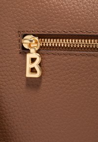 Pelle marrone testurizzata con una cerniera dorata e un'etichetta dorata prominente a forma di lettera "B" attaccata al tirazip.