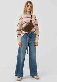 Brązowa skórzana torba na ramię noszona na kremowym swetrze w różowe paski i luźnych niebieskich dżinsach. Charakterystyczne szerokie nogawki i sznurek ściągający.