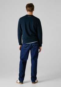 Marineblå genser med rund hals, kombinert med mørkeblå jeans. Hvite detaljer synlige ved kanten. Lyse sko fullfører antrekket.