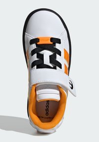 Sneaker blanc avec des lacets noirs, des accents orange et une sangle Velcro. Dispose d'une semelle texturée et d'une marque brodée.