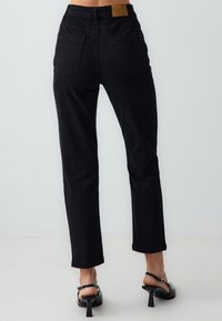 Jeans neri a vita alta con gamba dritta slim, design a cinque tasche e una toppa in pelle marrone nella parte posteriore della vita.