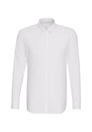 Homme portant une chemise blanche ajustée à manches longues boutonnée, rentrée dans un pantalon noir, les mains dans les poches.