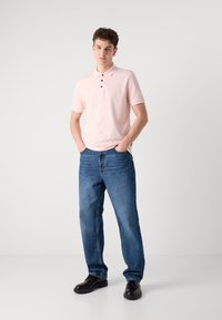 Ανοιχτό ροζ πόλο μπλουζάκι με τρία κουμπιά, συνδυασμένο με μπλε τζιν παντελόνι και μαύρα παπούτσια. Απλός σχεδιασμός με απαλή υφή και άνετη εφαρμογή.