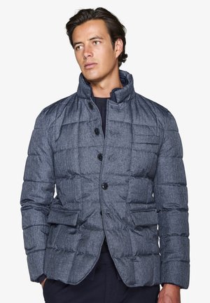 Chaqueta acolchada de color azul oscuro con cuello alto, cierre de botón y dos bolsillos frontales. Tejido texturizado con un patrón acolchado.