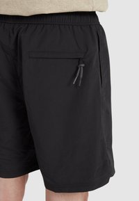 Shorts neri con un elastico in vita, tasche laterali con chiusura a zip e un tessuto leggero e liscio.