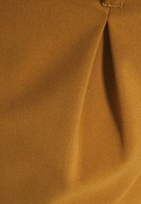 Texturovaná látka v spálené oranžové, s detailem skládaní, vyzdvihující hladký povrch a konzistentní barvu.