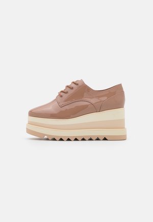 Chaussures compensées en cuir verni marron avec une semelle crème superposée, dotées d'un bout rond et d'un design classique à lacets. Semelle extérieure avec texture en zigzag.