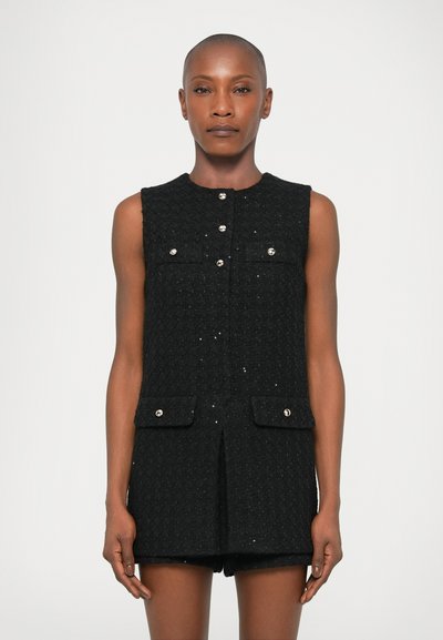 Tunic nera senza maniche con tessuto testurizzato, caratterizzata da due tasche frontali e bottoni argentati. Taglio dritto e lunghezza al ginocchio.