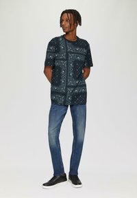 Korte mouwen, donkerblauw shirt met een witte bandana print, gecombineerd met lichtblauwe jeans en zwarte sneakers. Eenvoudig ontwerp, casual pasvorm.