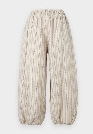 Pantalon beige ample avec des rayures noires verticales, taille élastique et poignets élastiques froncés aux chevilles.