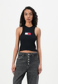 Black ribbed crop top with sleeveless design, featuring a colored logo patch that includes red, white, and blue sections.