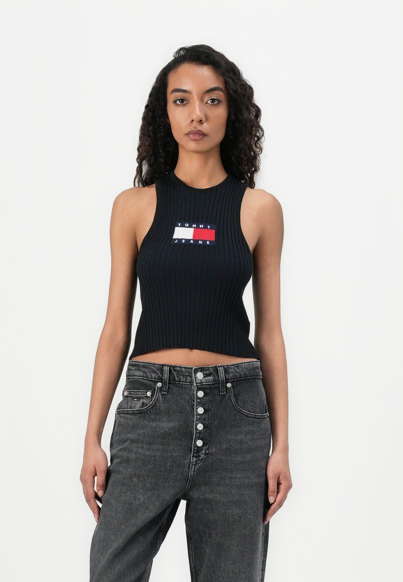 Black ribbed crop top with sleeveless design, featuring a colored logo patch that includes red, white, and blue sections.