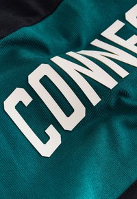 Close-up of green fabric with large white letters spelling "CONNE" on a textured, slightly wrinkled surface.