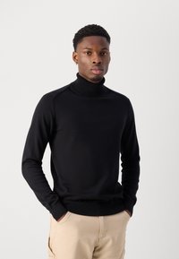 Suéter negro de cuello alto en un diseño ajustado, con cuello y puños acanalados, hecho de un suave y liso tejido de punto.
