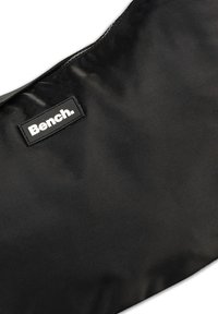 Zwarte nylon handtas met een gladde textuur, voorzien van een klein rechthoekig logoplaatje met de tekst "Bench." in witte letters.