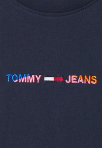 Camiseta de color azul marino oscuro con texto bordado multicolor "TOMMY - JEANS" y un acento rectangular tricolor entre las palabras.