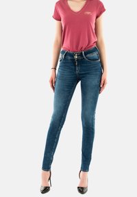 T-shirt rose en V associé à un jean en denim bleu ajusté. Le jean présente un design classique à cinq poches et est complété par des escarpins noirs.