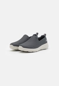 Chaussures grises à enfiler avec une tige en tissu en maille et des semelles en caoutchouc blanc. Les caractéristiques incluent une boucle au talon et une surface texturée pour la respirabilité.