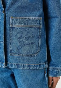 Lichtblauwe denimjacket met een borstzak met een reliëf "Pepe Jeans" logo. De stof heeft een gestructureerde afwerking en zichtbare stiksels.