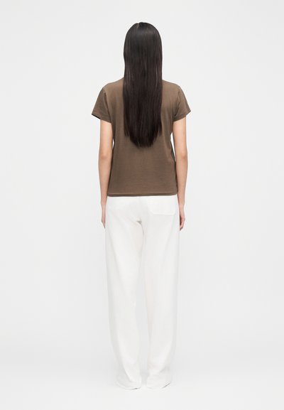 Barna rövid ujjú póló fehér bő szárú nadrággal, hátulnézetből. Az anyag puha, laza szabású.