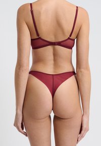 Burgunderfarbenes Lingerie-Set mit einem transparenten Bh und einem passenden String, beide mit minimalistischem Design und weichem Material.
