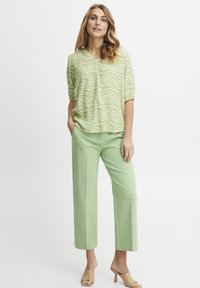 Top verde chiaro a fantasia con scollo a V e maniche corte, abbinato a pantaloni larghi verde pallido e sandali con tacco beige.