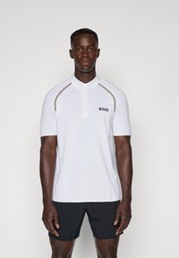 Polo shirt blanc à manches courtes, doté d'un col à trois boutons, de rayures d'accent noir et or, et d'un logo "BOSS" sur la poitrine.