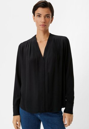Black long-sleeve blouse with a V-neck, subtle pleats at shoulders, smooth texture, and a relaxed fit, paired with blue jeans.