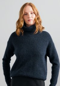 Marinblått ullhalsduk med avslappnad passform och texturerad yta. Har långa ärmar och hög krage. Standarddesign.
