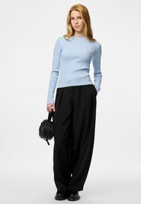 Gaiši zils ribots garām piedurknēm tops, apvienots ar augsto jostasvietu melniem plašiem bikšu. Modelis tur nelielu melnu strukturētu somiņu.