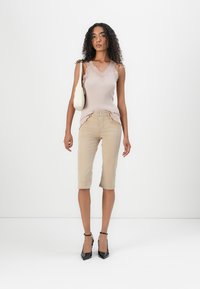 Top de alça bege com renda, combinado com calças cropped bege claras e sapatos de salto alto pretos. A segurar uma pequena bolsa branca.