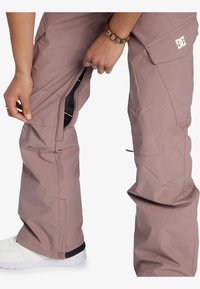 Rosa Schneehosen aus wasserdichtem Material verfügen über Reißverschlussbelüftungen an den Seiten und einen verstellbaren Saum mit einer sicheren Befestigung am Knöchel.