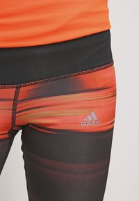Leggings de sport Adidas présentant un design dégradé orange et noir multicolore, une texture lisse, des coutures à surpiqûre et des détails de logo.
