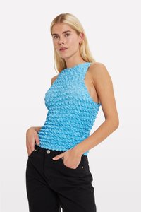 Világoskék, ujjatlan top, texturált, gyűrt anyagból. Magas nyakú, enyhén testhezálló fazonú. Fekete nadrággal párosítva.