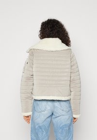 Szara pikowana kurtka z białym kołnierzem i mankietami z baranka. Posiada poziome przeszycia i dopasowane mankiety, zestawiona z jasnoniebieskimi wzorzystymi dżinsami.