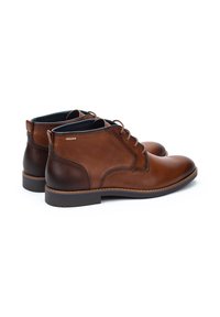 Botas de tobillo de cuero marrón con textura suave, punta redonda, detalles de cordones y tacón más oscuro en contraste. Suela de goma para mayor agarre.