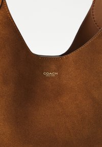 Brown suede handbag with a rounded top and visible stitching; "COACH NEW YORK" logo embossed in gold on the front.