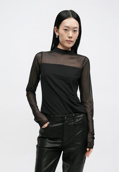 Čierny dlhý rukáv s priehľadnými sieťovinovými rukávmi a pevnou čiernou časťou tela, doplnený čiernymi lesklými nohavicami s vysokým pásom.