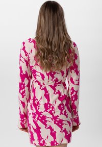 Lyhythihainen mekko vaalean kermanvärisenä, jossa on vaaleanpunainen abstrakti kuvio, vyötärö on kiristetty ja hame on levenevä, kankaan pinta on sileä.