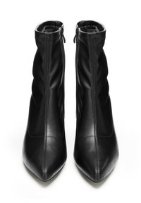 Paire de bottines à talons hauts en cuir noir avec des coutures verticales à l'avant et des fermetures éclair latérales, vues de face sur un fond blanc.